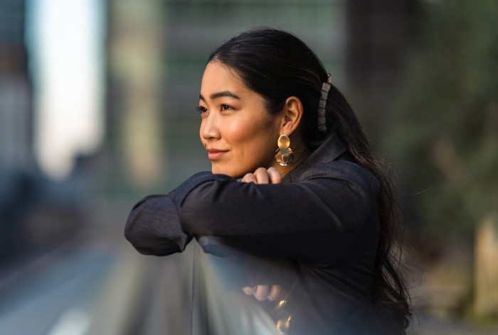 A woman with long, dark hair leans on a railing and gazes into the sunset.