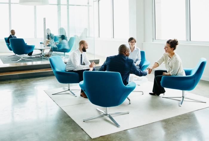 Four businesspeople sitting in armchairs at a meeting, celebrating a successful business deal.