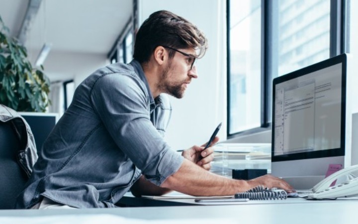 A man sits at his desk, working intently on something displayed on his monitor.