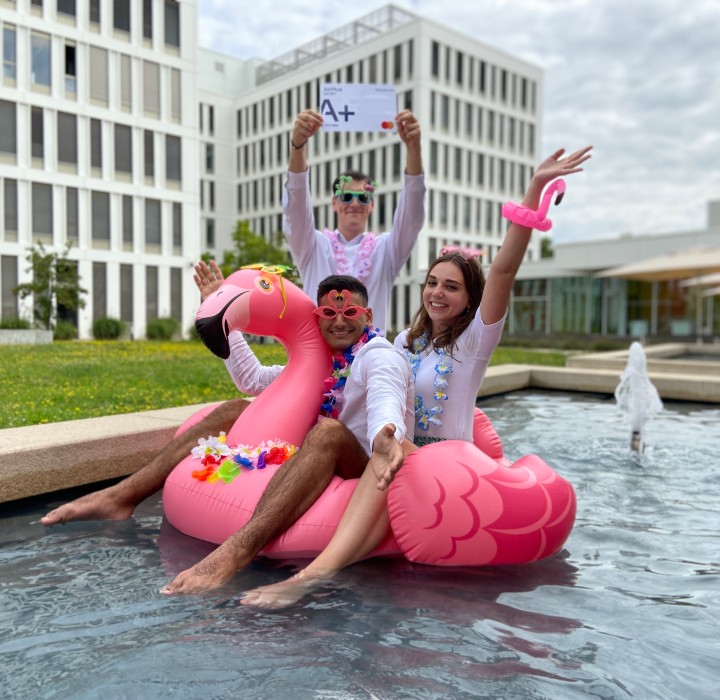 Three happy people sit on an inflatable flamingo in a pool of water and cheer.