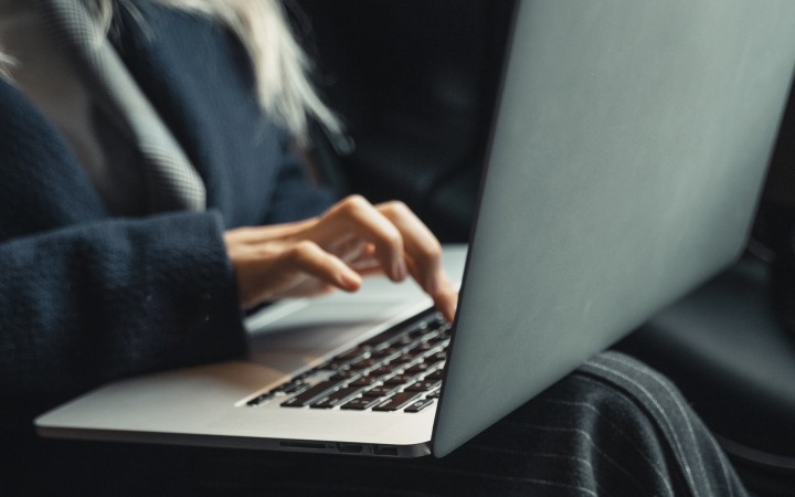 A woman has a laptop on her lap and is typing something.