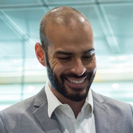 A businessman in a suit smiles and looks downward.